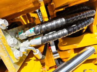 Close-up of hydraulic hoses and connectors on heavy machinery in bright sunlight, highlighting...