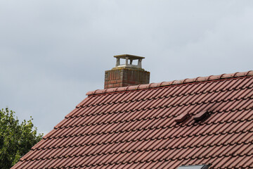 A traditional brick chimney on a weathered red terracotta tile roof of a residential house