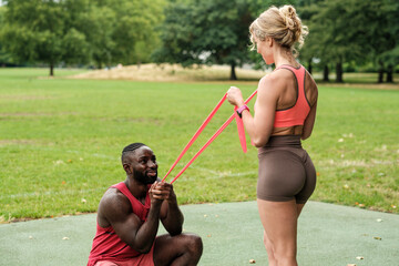 Personal trainer guiding client exercising with resistance band in park