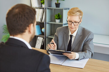 Serious woman in suit conducting hr interview meeting with candidate man, holding clipboard hiring...