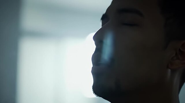 Close Up of Young Man Exhaling Smoke with White Background and Moody Lighting