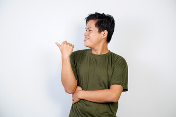 A young Asian man smiling cheerfully, feeling happy and pointing to the side, showing object in...