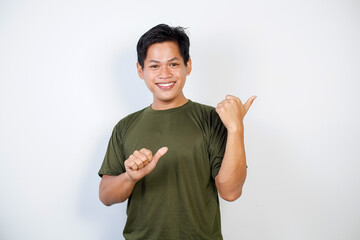 A young Asian man smiling cheerfully, feeling happy and pointing to the side, showing object in...