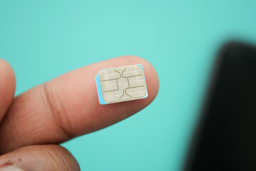 Tiny SIM card held between fingers against blue background