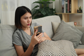 Portrait of Beautiful Asian woman in casual clothes relaxing on sofa and playing with mobile phone in living room at home. Holiday activity.