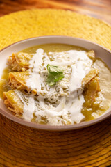 Green enchiladas. Typical Mexican dish made with a folded or rolled corn tortilla filled with shredded chicken and covered with spicy green sauce, cream, grated cheese and onion.