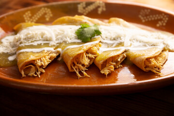 Green enchiladas. Typical Mexican dish made with a folded or rolled corn tortilla filled with shredded chicken and covered with spicy green sauce, cream, grated cheese and onion.
