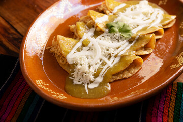 Green enchiladas. Typical Mexican dish made with a folded or rolled corn tortilla filled with shredded chicken and covered with spicy green sauce, cream, grated cheese and onion.
