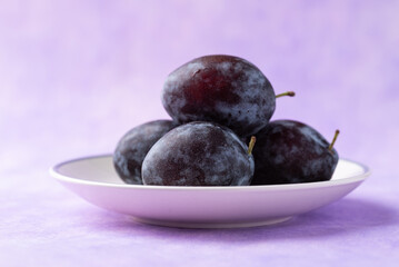 Fresh blue plum fruit on white plate with purple background