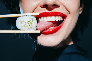 Smiling woman with red lips tasting sushi, showcasing joy and enthusiasm in a modern setting with a dark background.