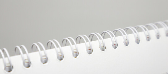 A close-up, abstract shot of the white plastic spiral binding of a notebook or calendar against a simple, light gray background. The focus is on the repeating rings.