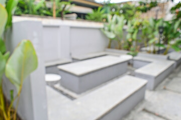 Blurred of empty grey or gray cement tables and chairs set in garden. Outdoor seating for restaurant, Cafe or coffee shop. Plants, green leaves, nature and wall. Background. nobody.