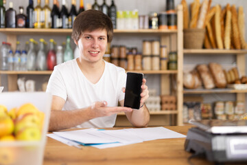 Man employee of shop store offers to download and install mobile application on phone. Stores website, applications, online purchases and reservations of fresh products in app