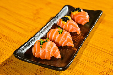 Close up view of mix salmon sushi on the long black plate. Wooden table. Traditional Japanese cuisine. Fish eggs.