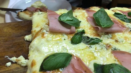 Argentinian fugazzeta pizza with cooked ham and basil leaves