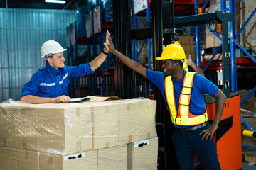 warehouse workers wearing helmets and reflective vests giving high five celebrating achievement...