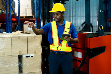 African male logistics employee standing near forklift giving directions using hand gestures while...
