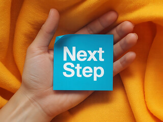 Hand holding a blue sticky note with next step written on it