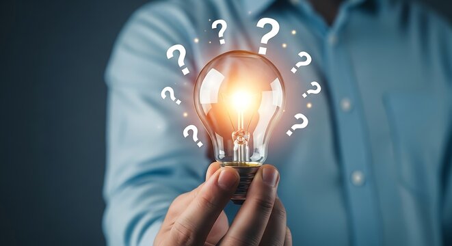 Person Holding Glowing Lightbulb Surrounded By Question Marks, Representing Innovation And Ideas.