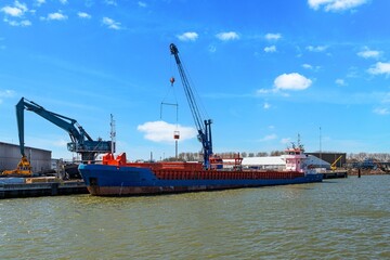 A cargo ship is being unloaded at a busy port with cranes working efficiently under a clear blue...