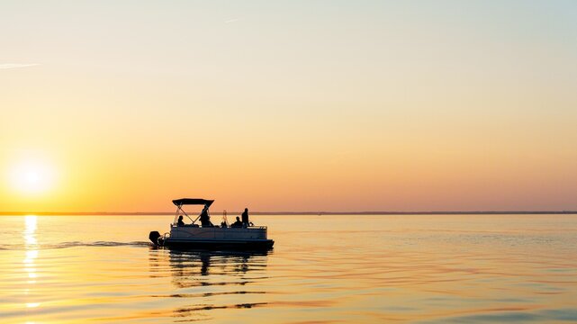Enjoy the serene beauty of a pontoon boat gliding on calm waters at sunset. Ideal for travel and relaxation themes, this image captures tranquility and peacefulness.