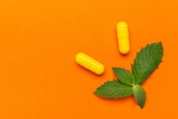 Yellow Capsules and Fresh Green Mint Leaves on Vibrant Orange Background