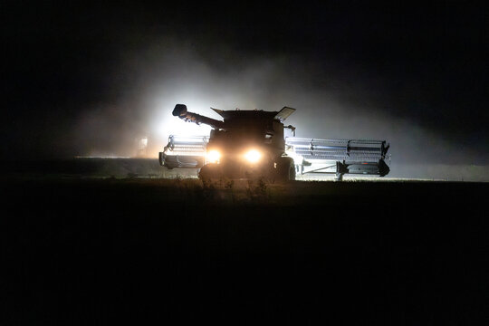 Harvester from behind reaping canola with dust and lights