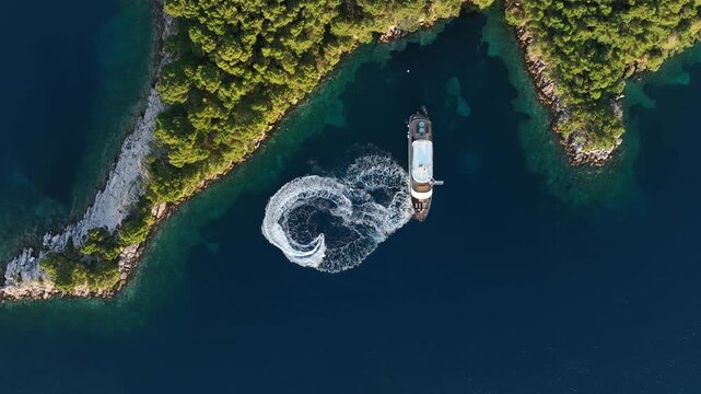 Jet ski makes circles by a yacht in a turquoise Croatian bay, top down aerial