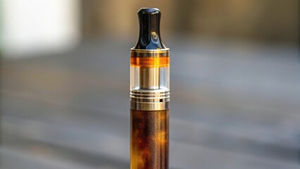 A close-up of a modern vape device with a metallic finish and a clear tank, set against a blurred background.