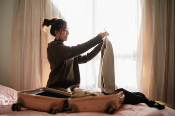 A woman packs a suitcase while preparing clothes, bathed in soft light, creating a cozy travel...