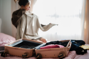 A person is packing a suitcase with clothes on a bed, preparing for a trip in a cozy, softly lit...