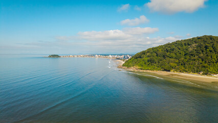 Aerial view of Guaratuba coastline with calm sea, sandy beach and green hill under a bright blue...