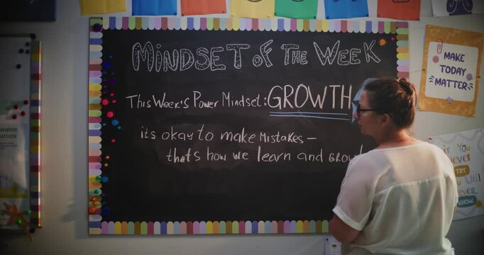 Female Teacher Wiping Motivational Message From Classroom Chalkboard, Finishing Psychology Lesson with Primary School Students. Woman Teaching Positive Mindset Building, Social and Emotional Learning.