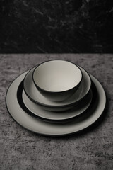 A minimalist monochrome dinnerware set. A stack of modern ceramic plates and a bowl in matte black and white on a gray textured background.