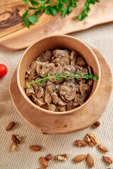 Deliciously Prepared Mushrooms in a Wooden Bowl Garnished with Fresh Thyme on a Textured Background with Nuts and Cherry Tomatoes