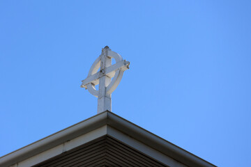 Weathered white cross on top of a church building against a clear blue sky background