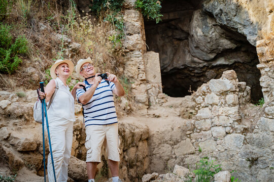 Senior couple tourists elderly people exploring ancient ruins with hiking poles, pensioners take pictures of the sights