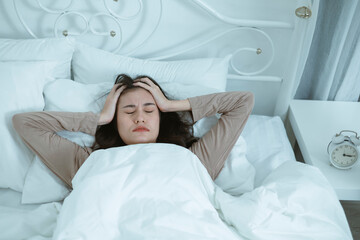 A young woman who wakes up in the middle of the night in bed with symptoms of anxiety, stress,...