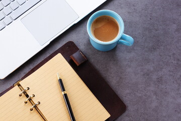 机にリング式のシステム手帳を広げ、淹れたてのコーヒー（カフェ・ラテ）を飲みながら、パソコンでデスクワークをしているイメージ
