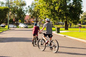 Young Aussie brothers on bikes with helmets riding away on road in country town