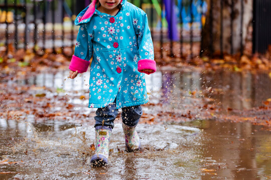 Little girl running and splashing through puddle filled with autumn leaves on rainy day