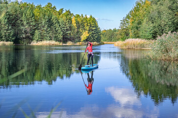 Active woman paddling SUP board on beautiful lake, autumn forest landscape and nature on...