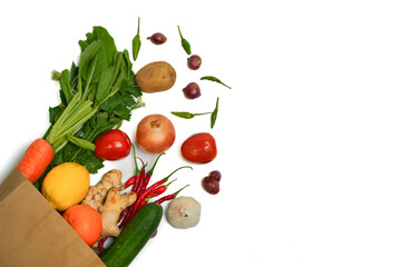 Reusable paper bag with fresh vegetables and spices: carrot, greens, celery, tomato, potato, ginger, chili, lemon, orange, cucumber on white background. Concept of eco-friendly and plastic-free.