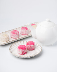 Homemade Chinese snow skin mooncakes. Snowy Moon cakes with Rose Bud Tea and White Teapot on White Background. Mid-Autumn Festival, traditional Asian desserts, and seasonal celebrations in Asian count