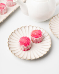 Homemade Chinese snow skin mooncakes. Snowy Moon cakes with Rose Bud Tea and White Teapot on White Background. Mid-Autumn Festival, traditional Asian desserts, and seasonal celebrations in Asian count