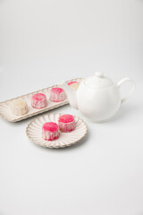 Homemade Chinese snow skin mooncakes. Snowy Moon cakes with Rose Bud Tea and White Teapot on White Background. Mid-Autumn Festival, traditional Asian desserts, and seasonal celebrations in Asian count