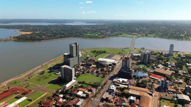 Panoramic aerial movement over the Encarnaci&oacute;n city buildings along Paran&aacute; river with Puente Mboi Ca'e bridge, Itap&uacute;a, Paraguay.