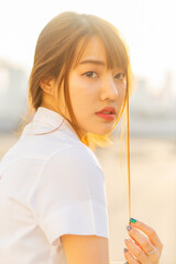 A close-up of a female student in uniform standing quietly on a rooftop, with the warm light of her...