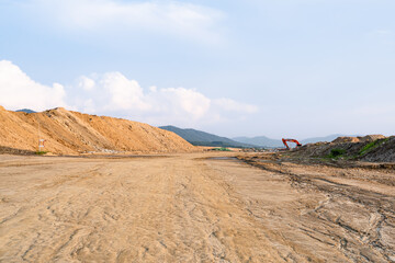 Expansive construction site with exposed earth and heavy machinery tracks. Surrounded by distant mountains, the scene captures early stages of land development and earthmoving operations.