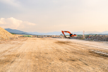 Expansive construction site with exposed earth and heavy machinery tracks. Surrounded by distant...